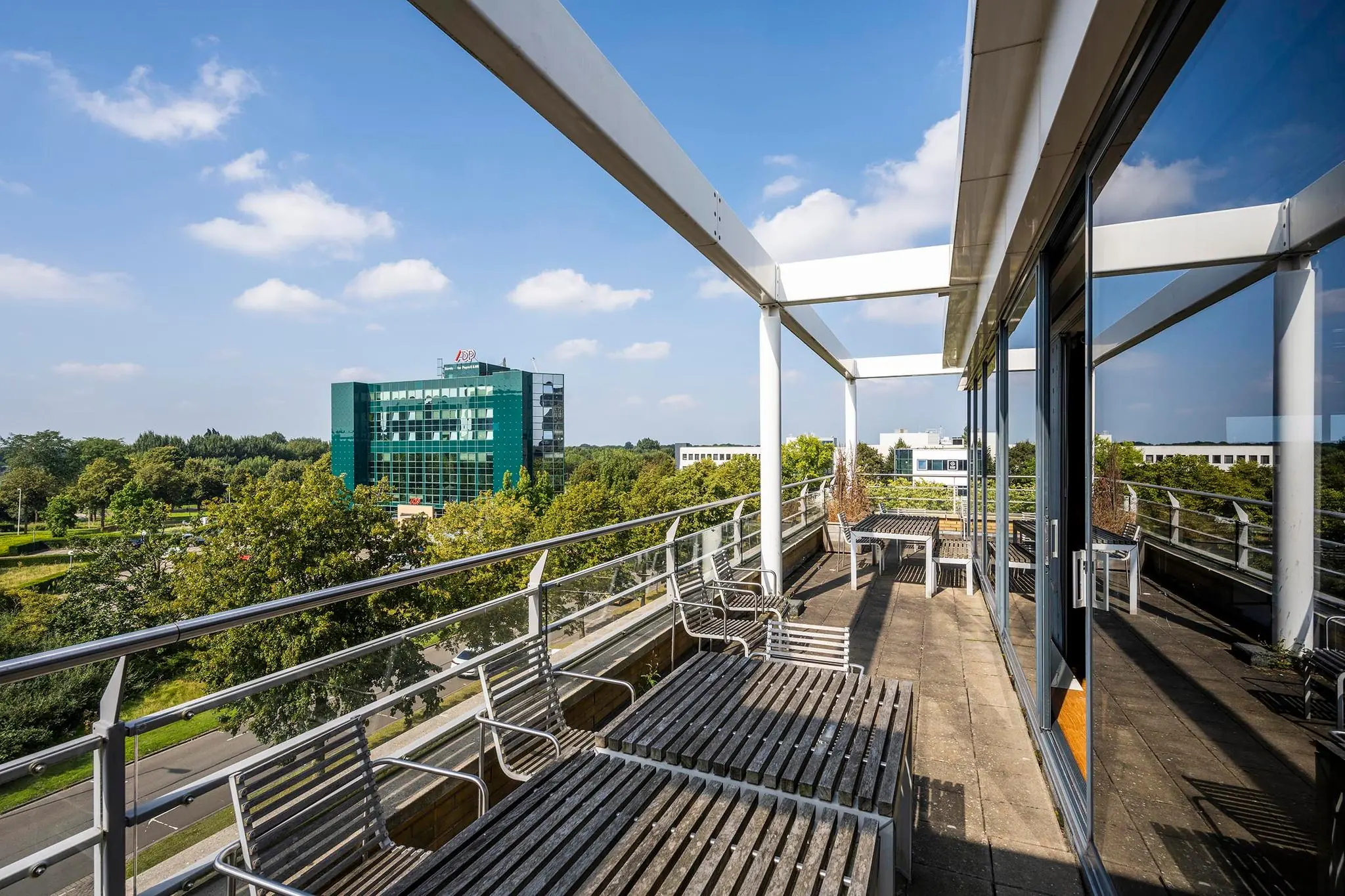 Ruim balkon met houten bankjes en uitzicht op het groene kantoorgebouw aan de K.P. van der Mandelelaan in Rotterdam.